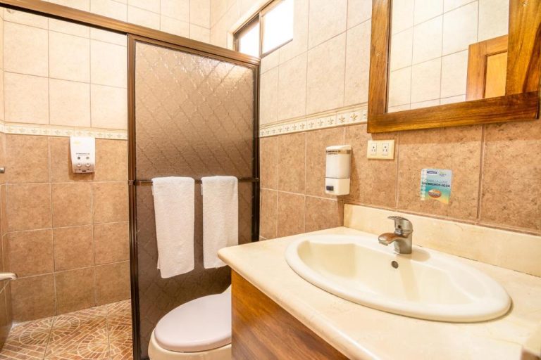 Baño privado con ducha de vidrio, lavabo y toallas blancas en el Hotel Pacuare