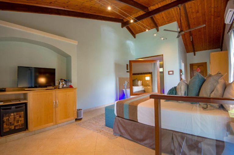 Habitación suite de lujo con cama doble, televisor y techo de madera en Coco de Mer Hotel Seychelles
