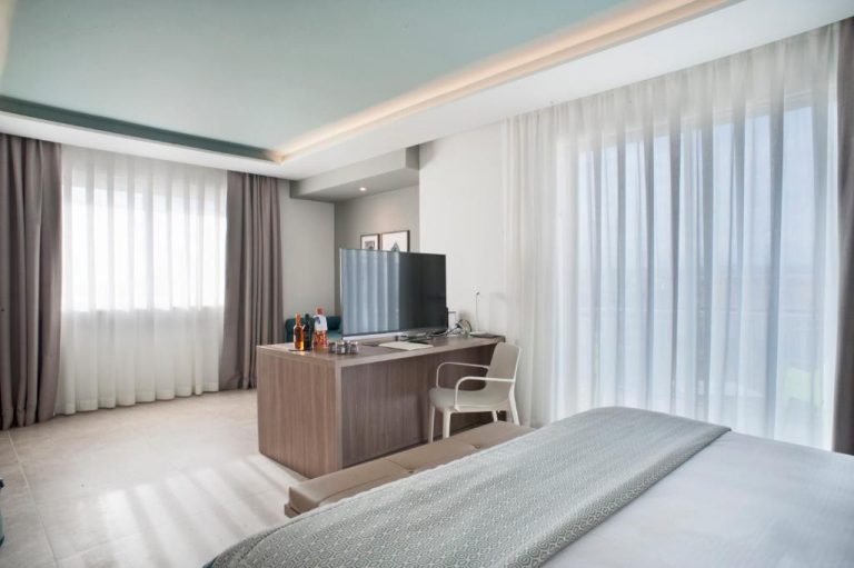 Habitación doble moderna con escritorio, televisión y amplias ventanas en Modica Beach Resort