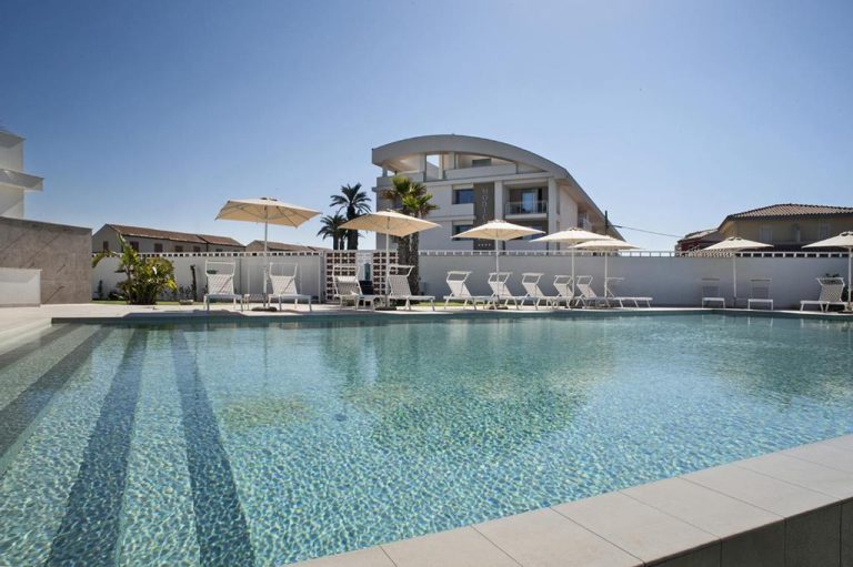 Piscina exterior con tumbonas y sombrillas blancas del Modica Beach Resort en Sicilia