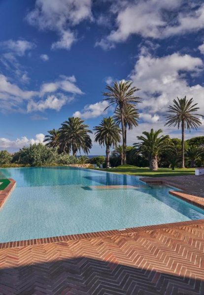 Piscina infinita exterior con palmeras y vistas al mar del Hotel Porto Santo & Spa