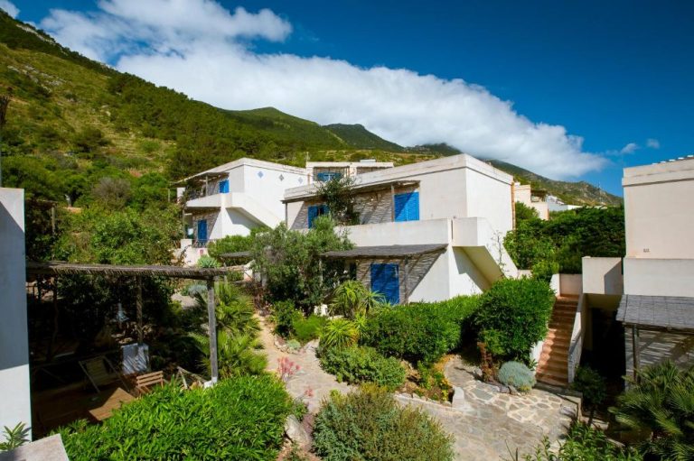 Jardín mediterráneo con vistas a la montaña y fachada blanca del Marettimo Residence en Sicilia