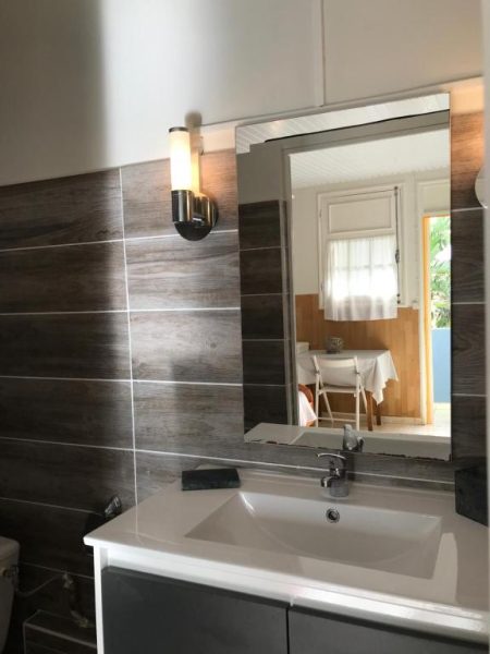 Baño moderno con lavabo blanco y espejo amplio en Hotel Oasis con decoración de azulejos efecto madera
