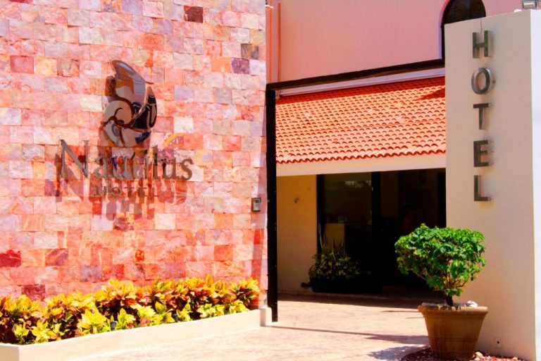 Fachada y entrada principal del Hotel Nautilus con logo en pared de piedra roja y jardines decorativos