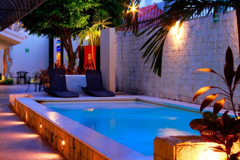 Piscina exterior iluminada de noche con tumbonas y jardín tropical en Hotel Nautilus