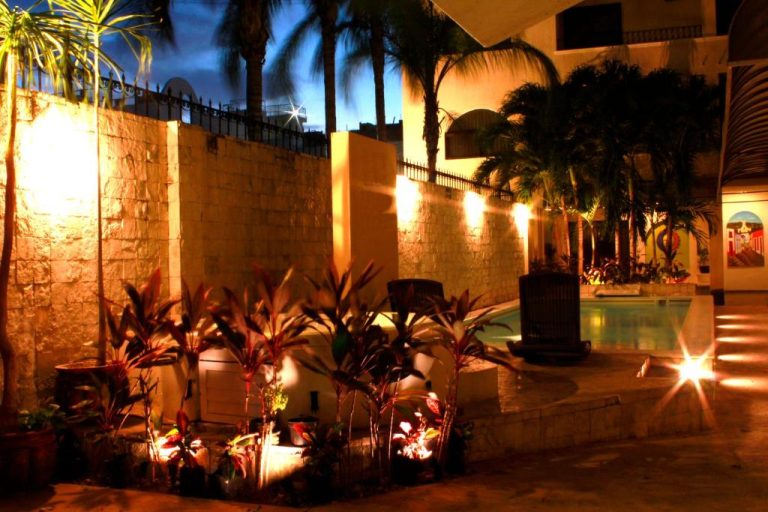 Jardín tropical iluminado con piscina exterior del Hotel Nautilus en una noche cálida