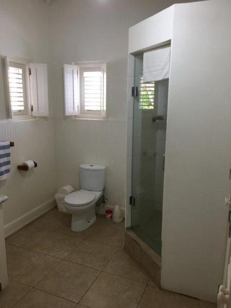 Baño privado con ducha de cristal y ventanas de persiana en The Atlantis Historic Inn