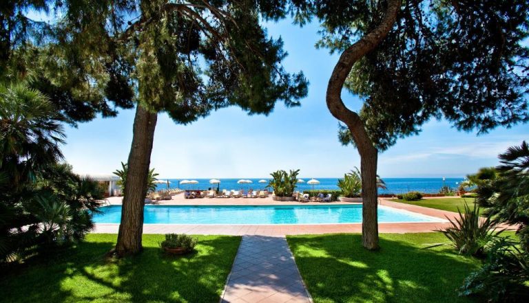 Piscina exterior con vistas al mar del Grand Hotel Baia Verde rodeada de jardines y palmeras