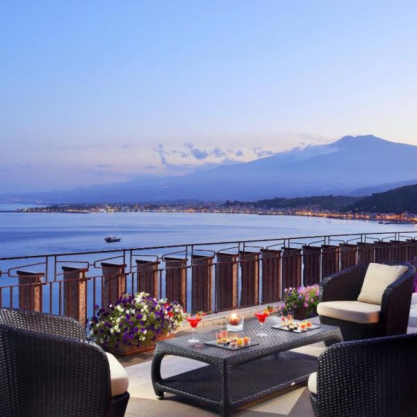 Terraza con sofás de ratán y vistas al mar y al Etna en UNA Hotels Capotaormina, Sicilia