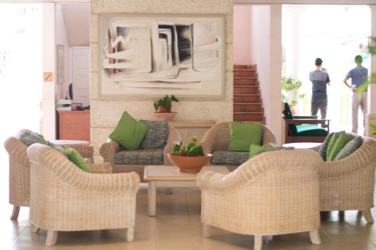 Sala de estar con sillones de mimbre y cojines verdes en el lobby del Hotel PomMarine