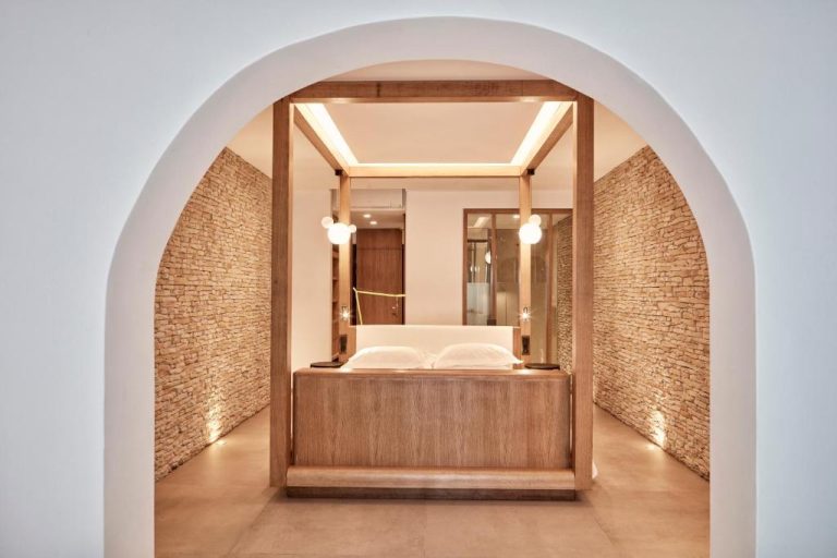 Habitación con cama de dosel de madera y paredes de piedra bajo arco en Myconian Naia Hotel