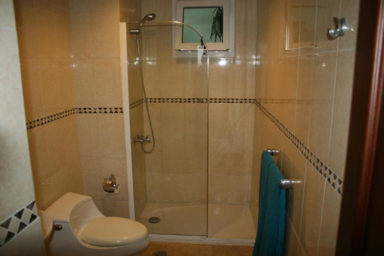 Baño con ducha de cristal, inodoro y toalla azul en el hotel Bavaro Green