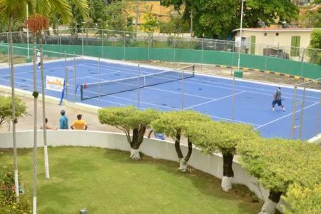 Pista de tenis exterior de color azul en SandCastles Holiday con jugadores y zona ajardinada