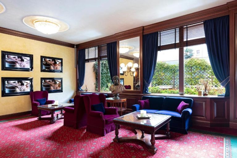 Elegante salón lounge clásico con sofás azules y sillones burdeos en Royal Hotel Carlton