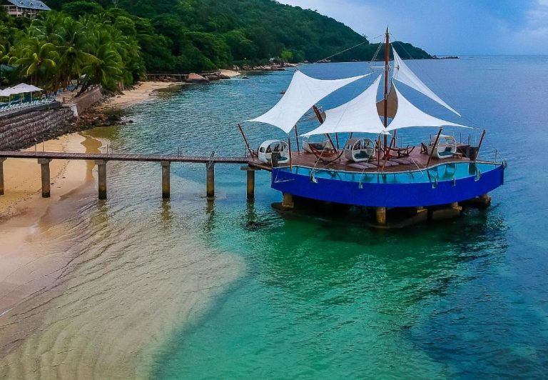 Muelle sobre el mar con bar flotante y velas blancas del Coco de Mer Hotel en Seychelles