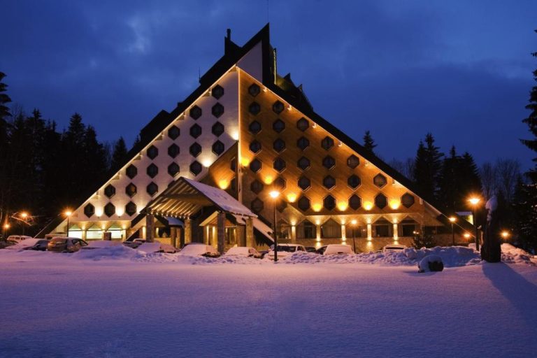 Fachada exterior iluminada del Bianca Resort & Spa en invierno con gran manto de nieve y arquitectura triangular