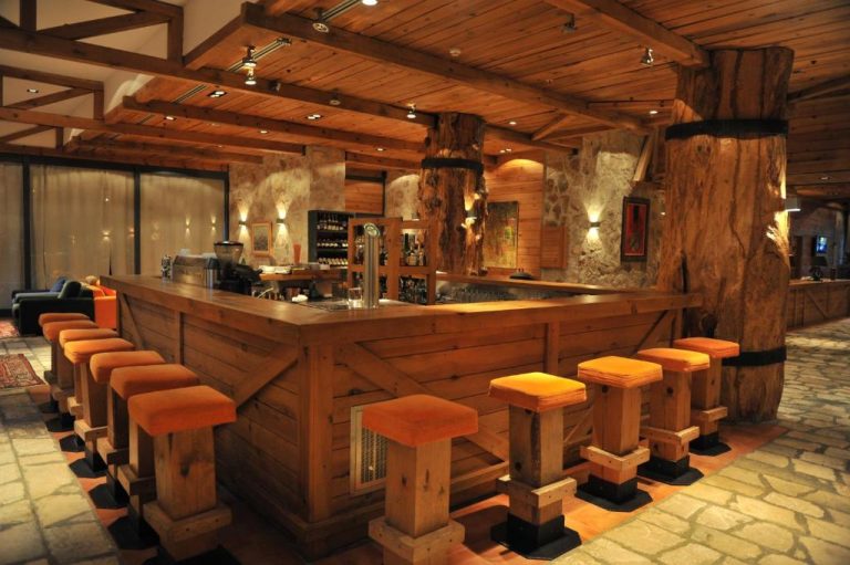 Bar rústico de madera con taburetes naranjas y columnas naturales en el Bianca Resort & Spa