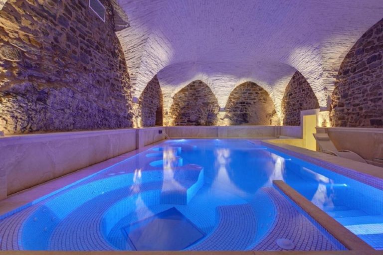 Piscina interior con bóveda de piedra medieval e iluminación azul en el spa del Monastero di Cortona Hotel & Spa
