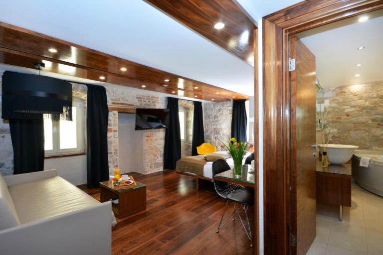 Suite de lujo con paredes de piedra, suelo de madera y bañera exenta en Jupiter Heritage Hotel