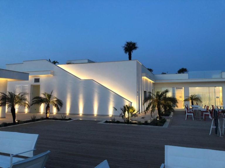 Terraza exterior iluminada del Modica Beach Resort con palmeras y zona de descanso al atardecer