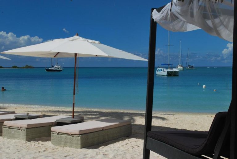 Playa privada del Voco Surfside Aruba con tumbonas, sombrilla blanca y veleros en el mar turquesa