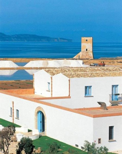 Vista exterior del Relais Antiche Saline con salinas blancas, torre histórica y mar azul al fondo en Sicilia