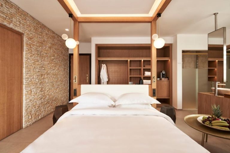 Habitación de lujo con cama doble y pared de piedra natural en Myconian Naia Preferred Hotels