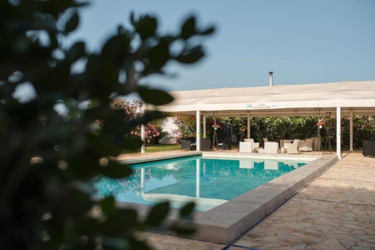 Piscina exterior con pérgola blanca y jardín de flores en el Relais Antiche Saline
