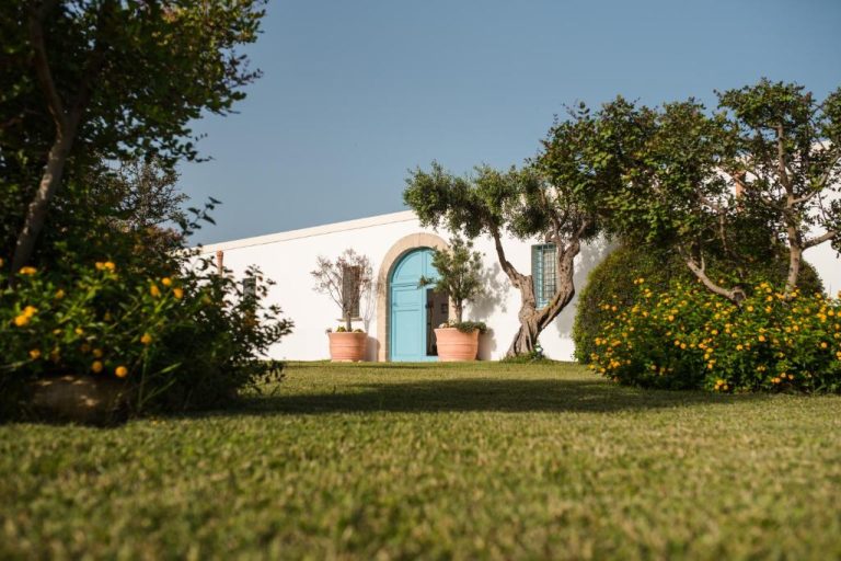 Jardín exterior con césped y puerta azul arqueada del Relais Antiche Saline en Sicilia