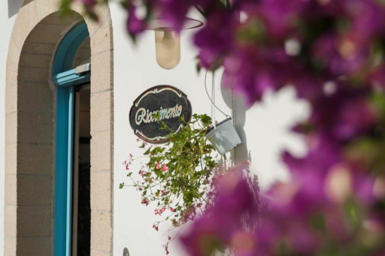 Fachada blanca con cartel y plantas colgantes del Relais Antiche Saline decorada con buganvillas rosas