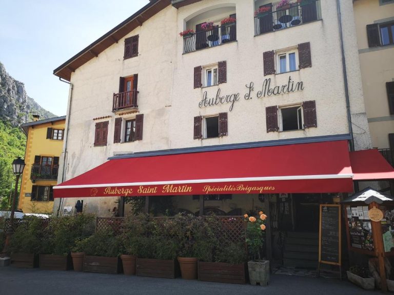 Fachada exterior del Auberge Saint Martin con toldo rojo y terraza con plantas en los Alpes