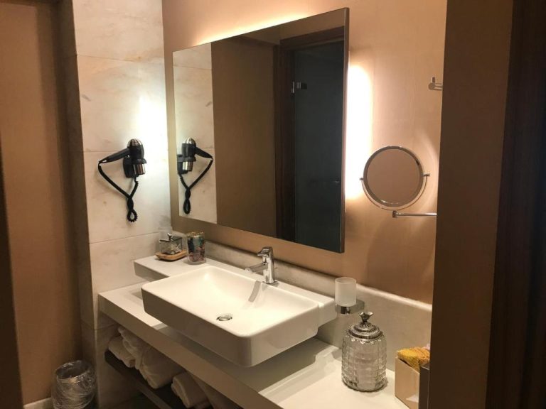 Baño moderno con lavabo blanco, espejo iluminado y secador de pelo del Hotel Levadia