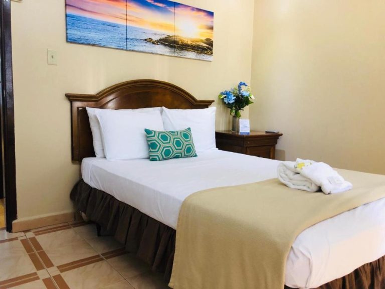 Habitación con cama doble y cabecero de madera en Arecibo Inn, decorada con cuadro de playa