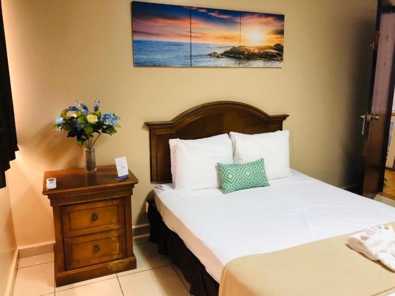 Habitación con cama doble y decoración de madera en Arecibo Inn, con cuadro de playa al atardecer