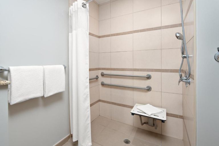 Baño accesible con barras de apoyo, asiento de ducha y teléfono de ducha en Courtyard Marriott Bridgetown Barbados