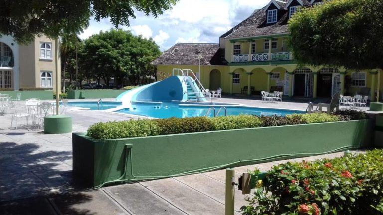 Piscina exterior con tobogán azul y área de descanso en SandCastles Holiday C9, rodeada de jardines