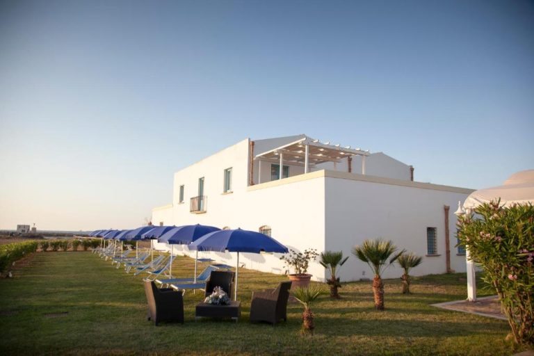 Jardín exterior con tumbonas y sombrillas azules del Relais Antiche Saline en Sicilia