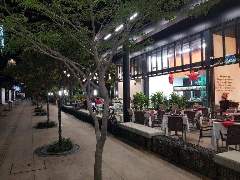 Terraza exterior del restaurante del Rivière Boutique Hotel iluminada de noche con mesas y árboles