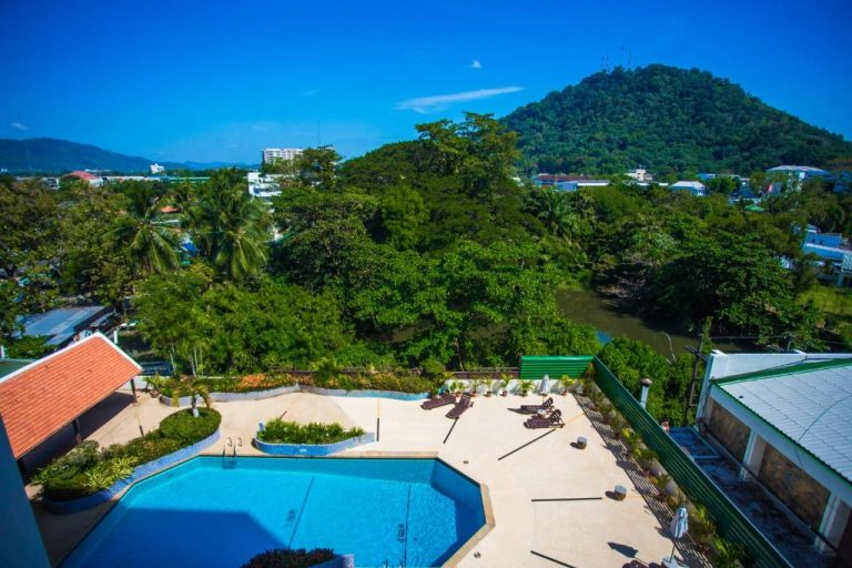 Piscina exterior con tumbonas y vistas a la montaña verde del Phuket Merlin Hotel en Tailandia