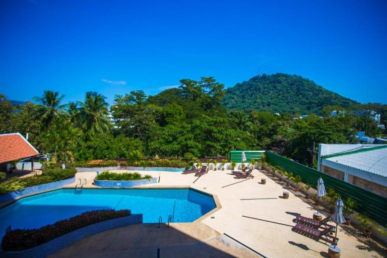 Piscina exterior con tumbonas y vistas a la montaña verde del Phuket Merlin Hotel en Tailandia