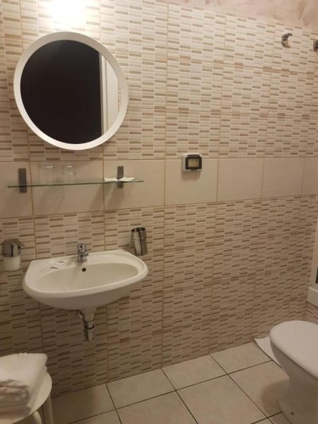 Baño moderno con lavabo, espejo circular y azulejos beige en el Hotel Biscari