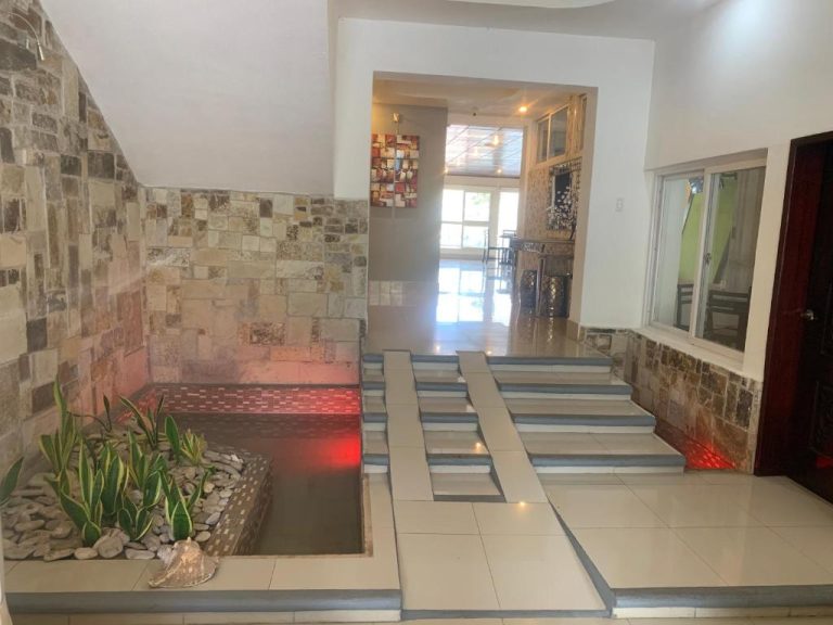 Lobby del Hotel Tijerinos con fuente decorativa, plantas tropicales y paredes de piedra natural iluminadas