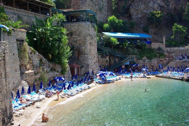 Playa privada con hamacas y sombrillas azules del Marka Hotel junto a acantilados rocosos