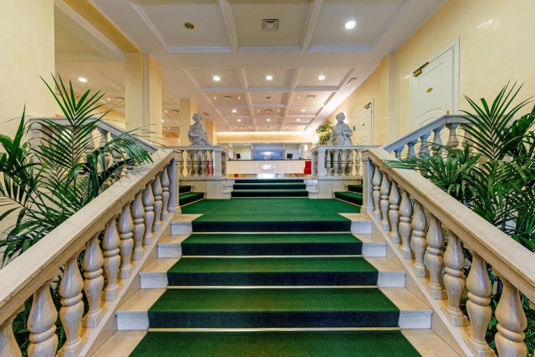 Escalera principal con moqueta verde y balaustrada de mármol en el lobby del Ambassador Palace Hotel