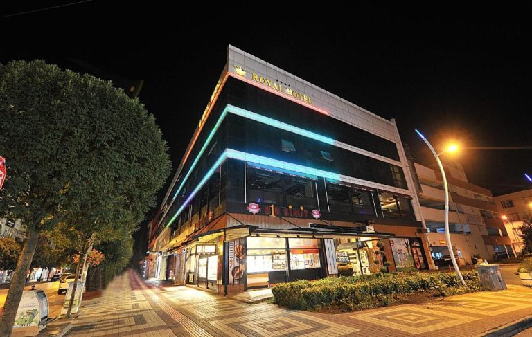 Fachada nocturna iluminada del Royal Hotel Inegol con luces de neón y tiendas en planta baja