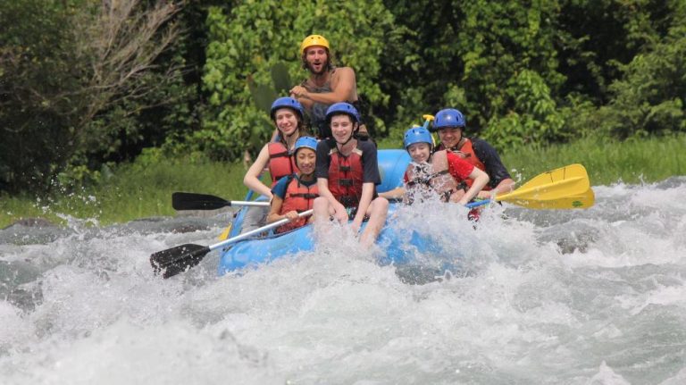 Grupo de turistas practicando rafting en aguas bravas cerca del Hotel Villas Rio Mar con cascos y chalecos