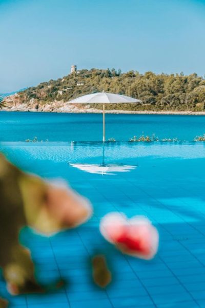 Piscina infinita con sombrilla blanca y vistas al mar turquesa en Hotel La Bitta Bovis Hotels