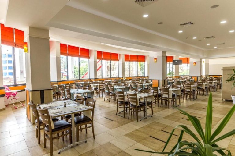 Amplio restaurante buffet con mesas dispuestas y ventanales con cortinas naranjas en Kuban Resort & Aquapark