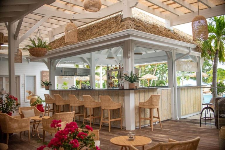 Bar tropical con techo de paja y taburetes de ratán en la terraza del Le Relais du Moulin Hotel Spa