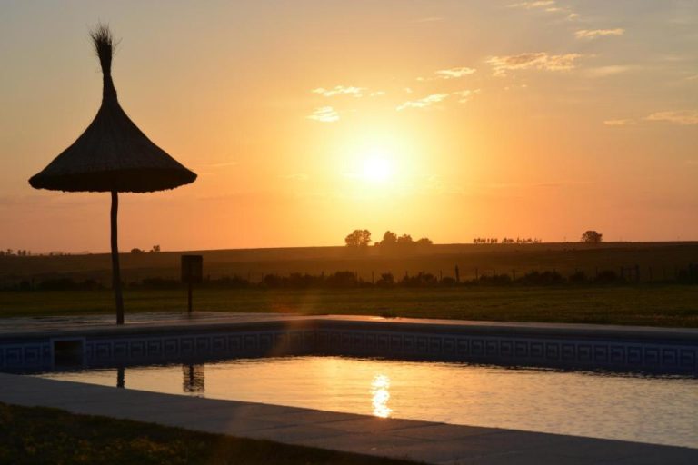 Piscina exterior con sombrilla de paja al atardecer en Hotel Santa Cristina con vistas al campo